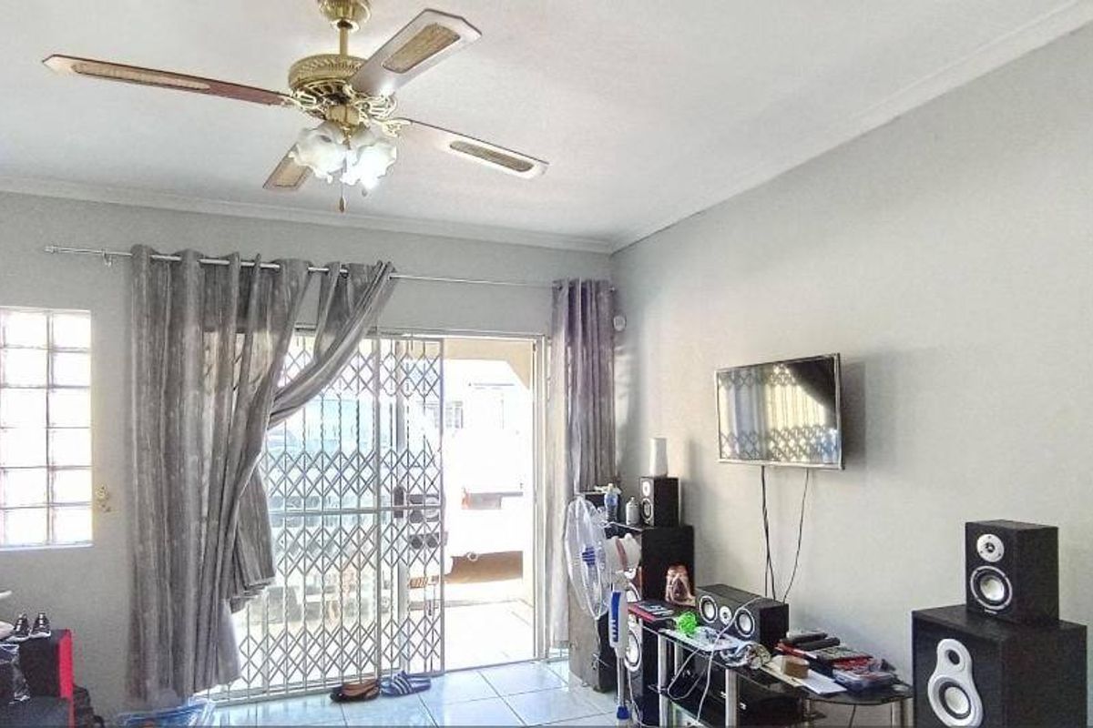 A living room featuring tiled flooring, a ceiling fan, a glass block window, and a sliding door with a security gate leading outdoors.