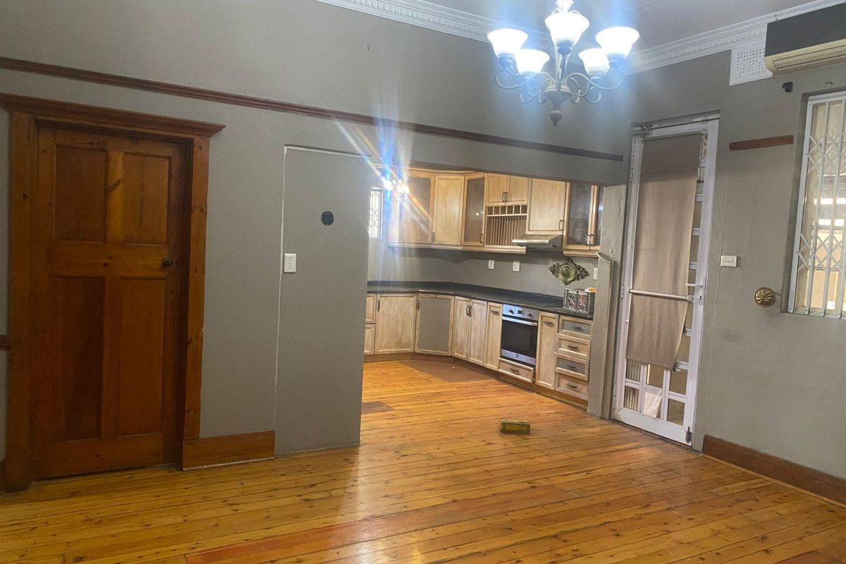 Open plan living area featuring timber flooring, crown molding, and a connected kitchen with built-in cabinetry, oven, and extractor fan.