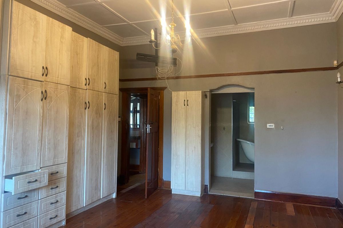 Spacious bedroom featuring extensive built-in cabinetry, original hardwood flooring, and decorative ceiling details, with an adjoining en-suite bathroom area.