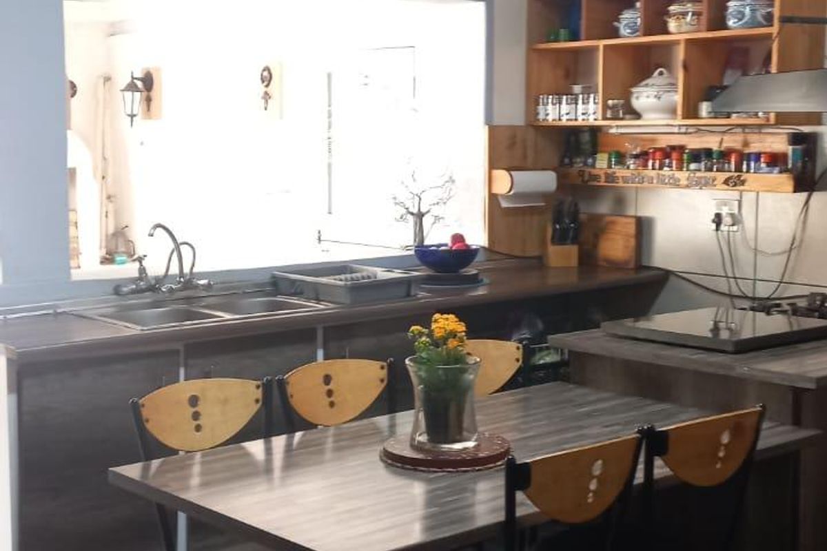 A functional kitchen featuring dark tiled flooring, laminate countertops, double sink, and open shelving with a pass-through window to the adjacent living area.