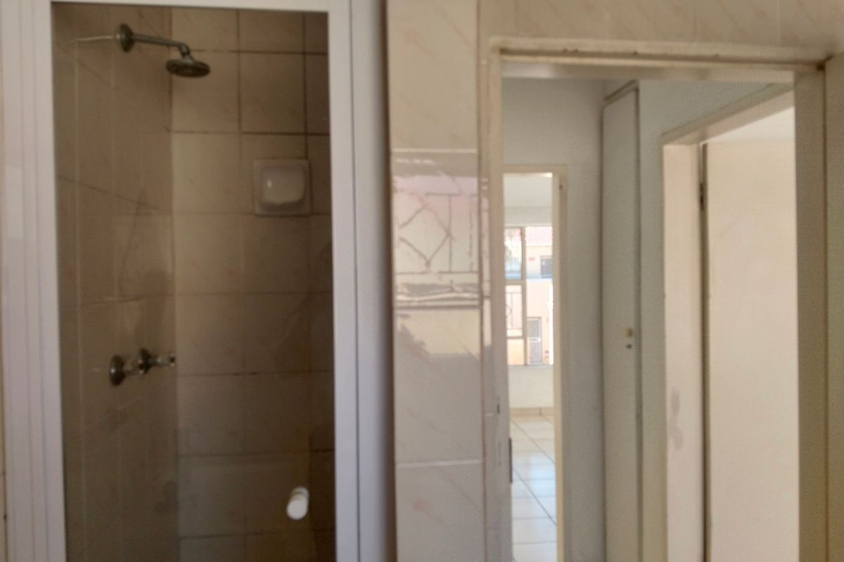 A dated bathroom featuring a shower enclosure with tiled walls, leading into a hallway with built-in storage.