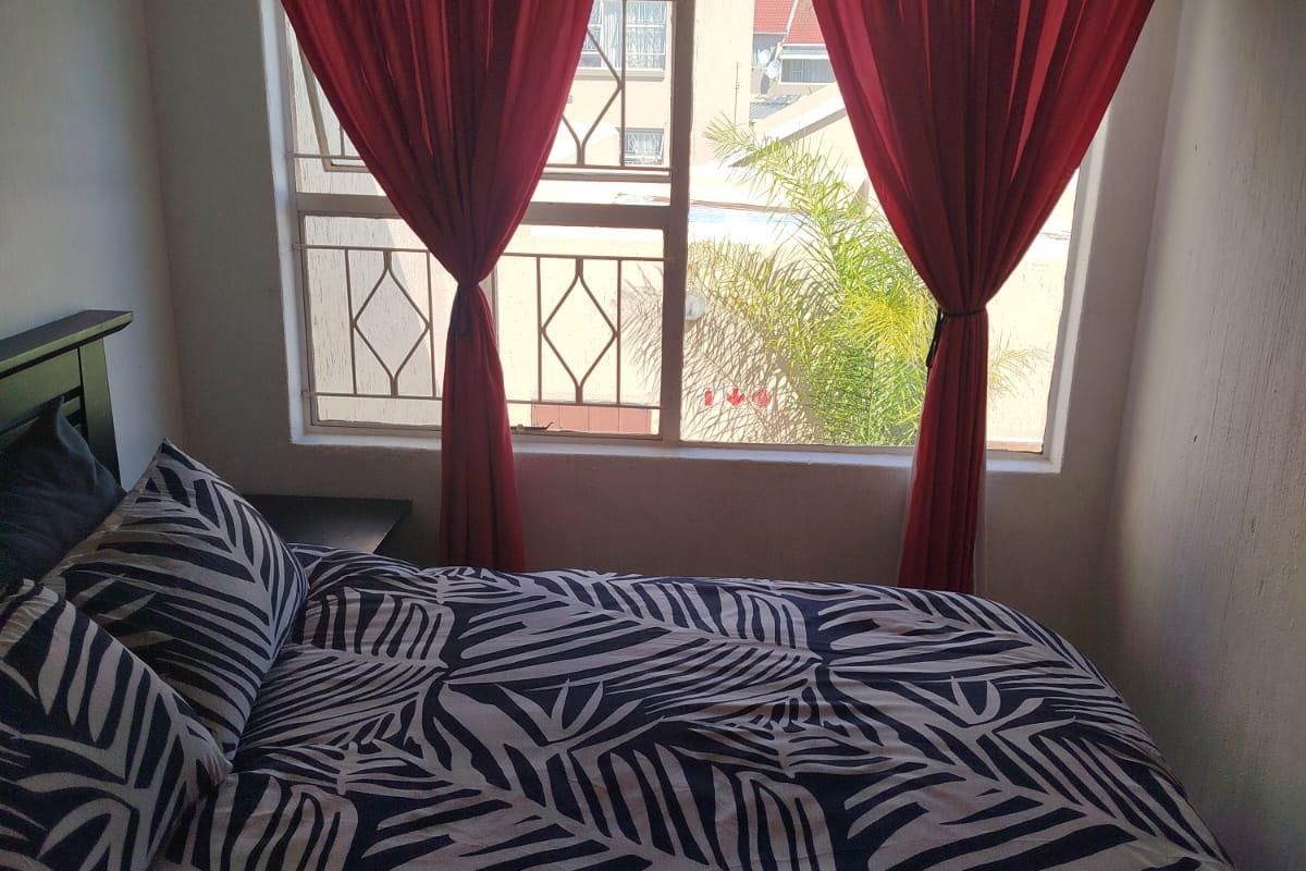 A compact bedroom featuring a window with security bars, providing natural light and a view of the surrounding residential area.