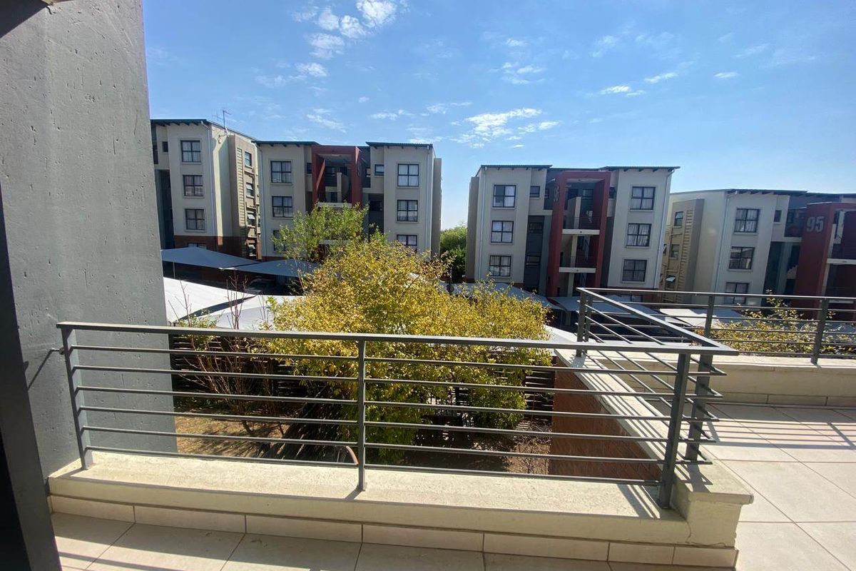 A spacious balcony featuring tiled flooring and a modern metal balustrade, offering an elevated view of the surrounding apartment complex.