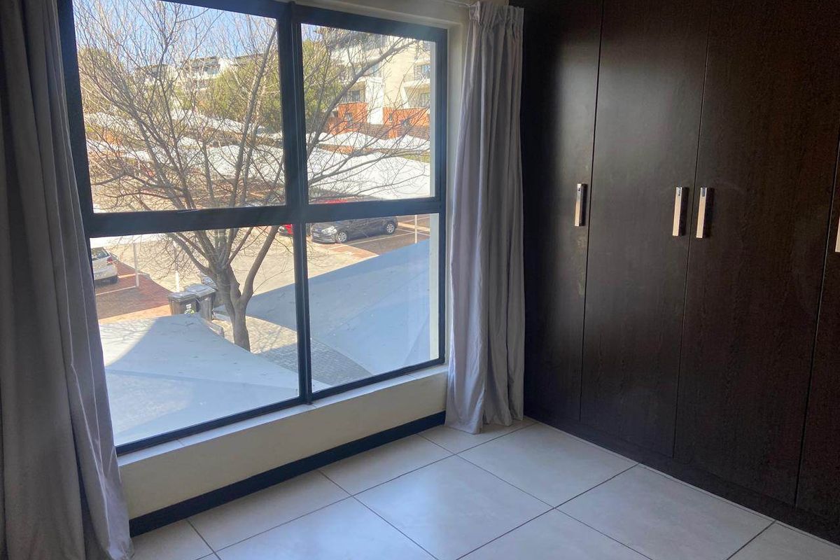A bright, empty bedroom featuring tiled flooring and dark built-in cupboards, offering a view of the complex exterior.