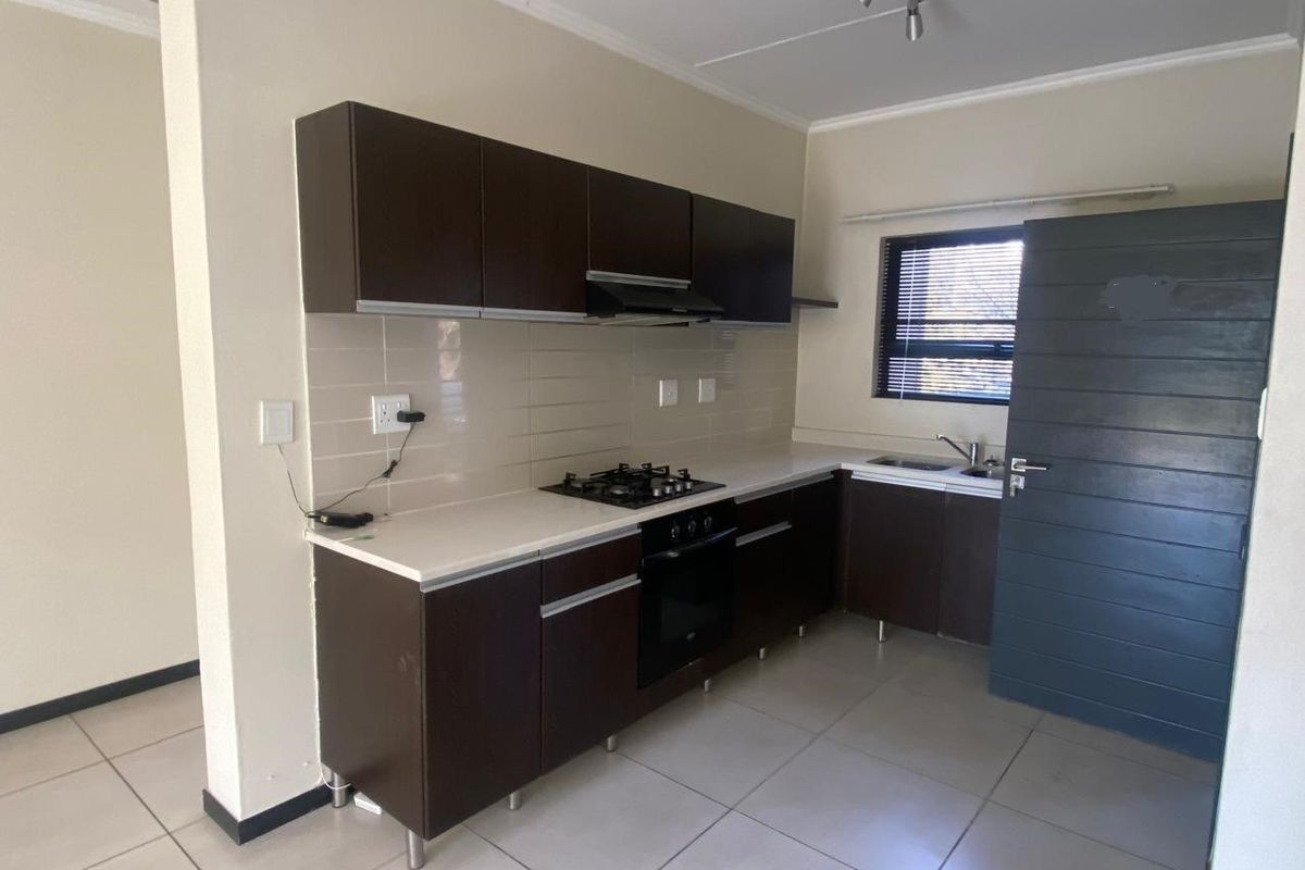 A clean, functional kitchen featuring dark wood cabinetry, a gas hob, built-in oven, and tiled flooring, offering a practical layout for daily use.