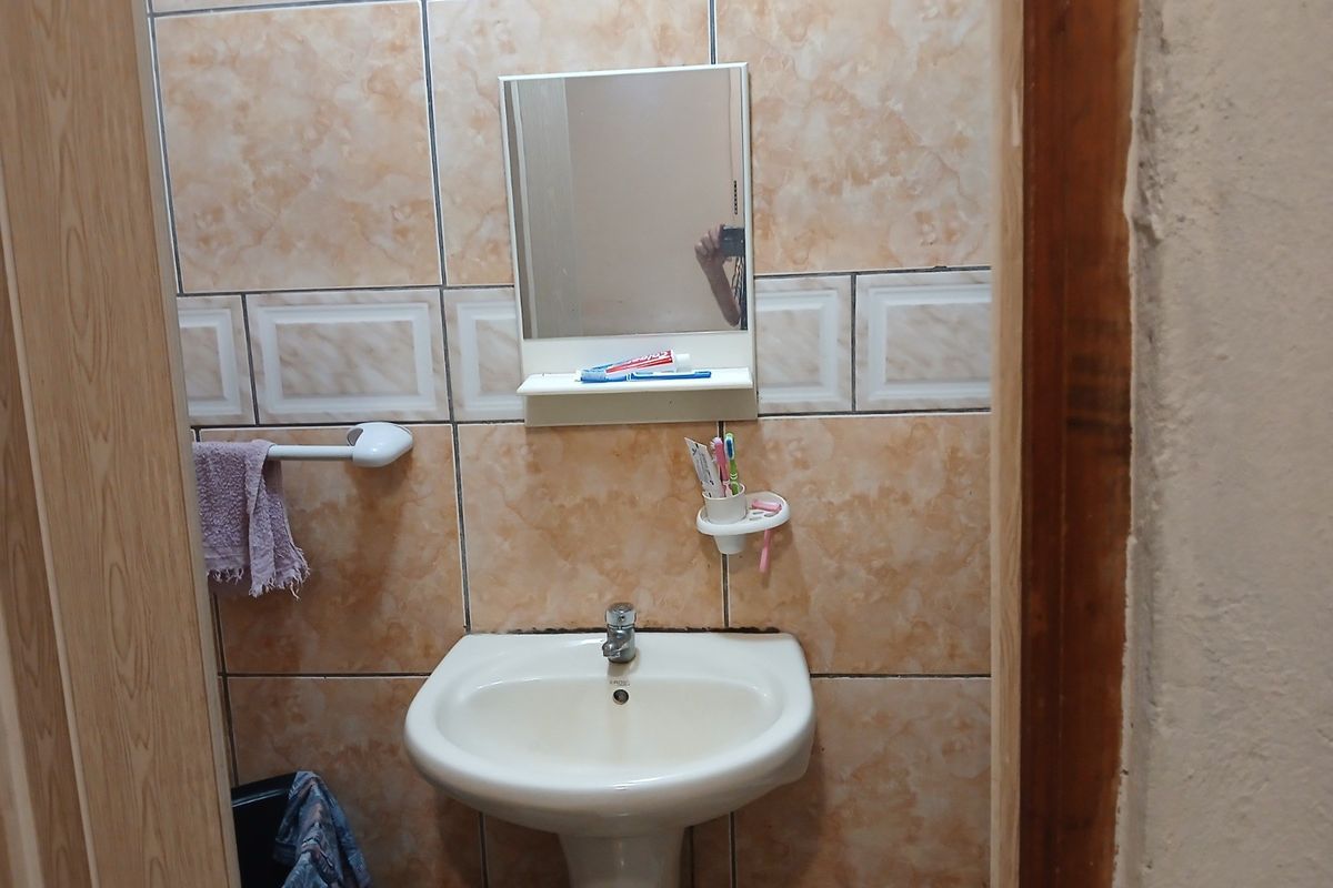 A compact bathroom featuring a pedestal basin, wall-mounted mirror, and tiled wall finishes.