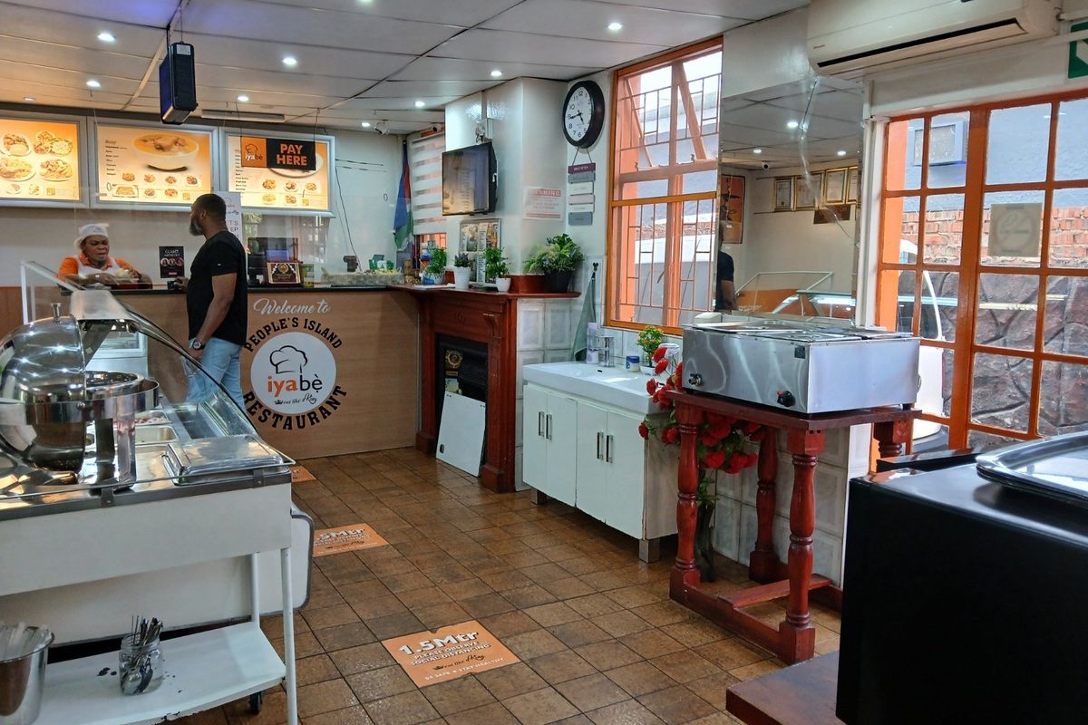 A commercial kitchen space featuring tiled flooring, built-in service counters, cabinetry, and wall-mounted air conditioning, currently set up for restaurant operations.