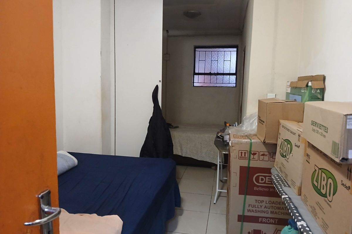 A compact bedroom featuring tiled flooring, a built-in wardrobe, and a window fitted with security bars.