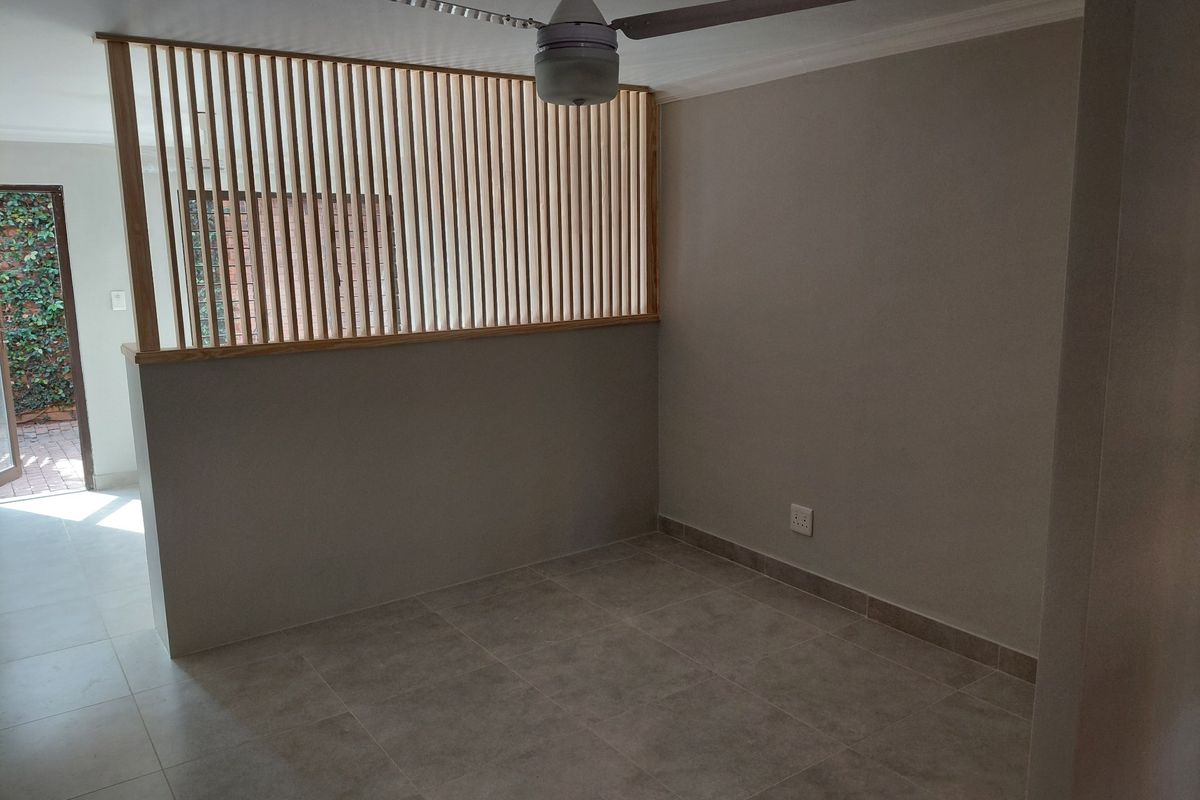 An empty living area featuring neutral tiled flooring, a modern ceiling fan, and a decorative timber slat room divider.