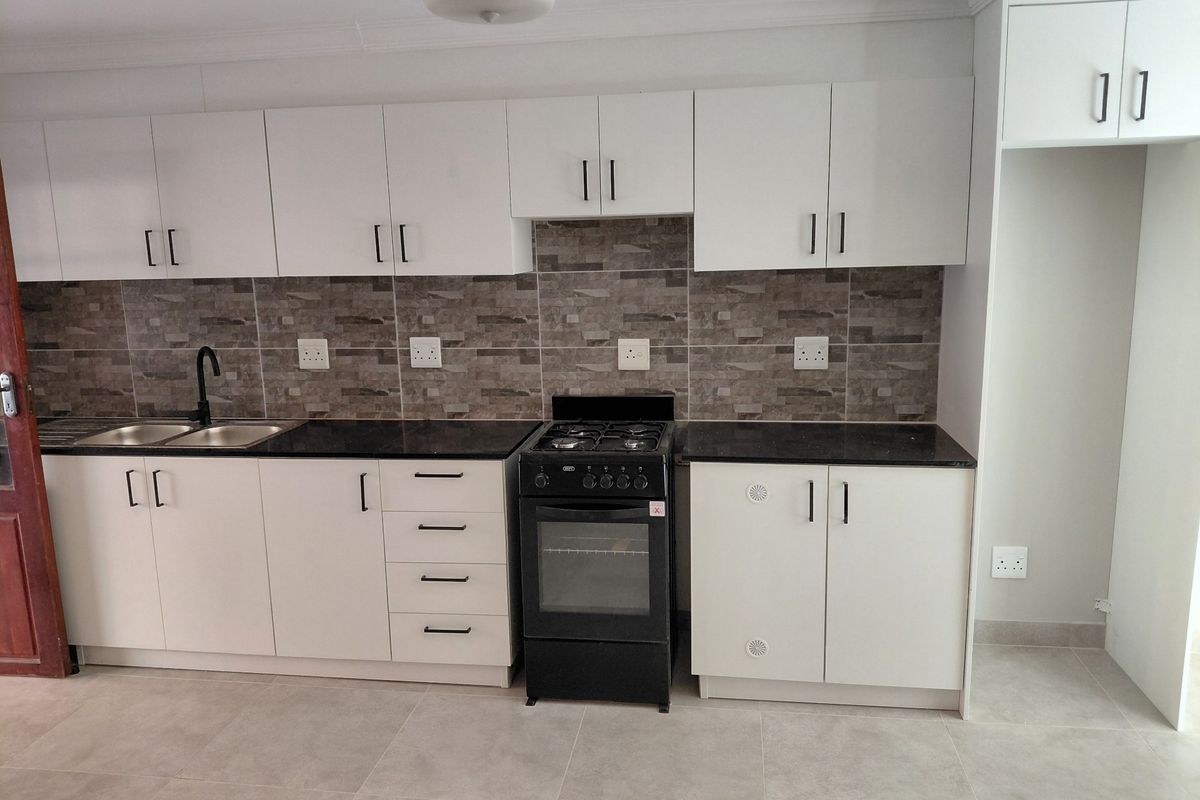 Modern kitchen featuring white cabinetry, dark stone countertops, a tiled backsplash, and a freestanding gas stove with oven.