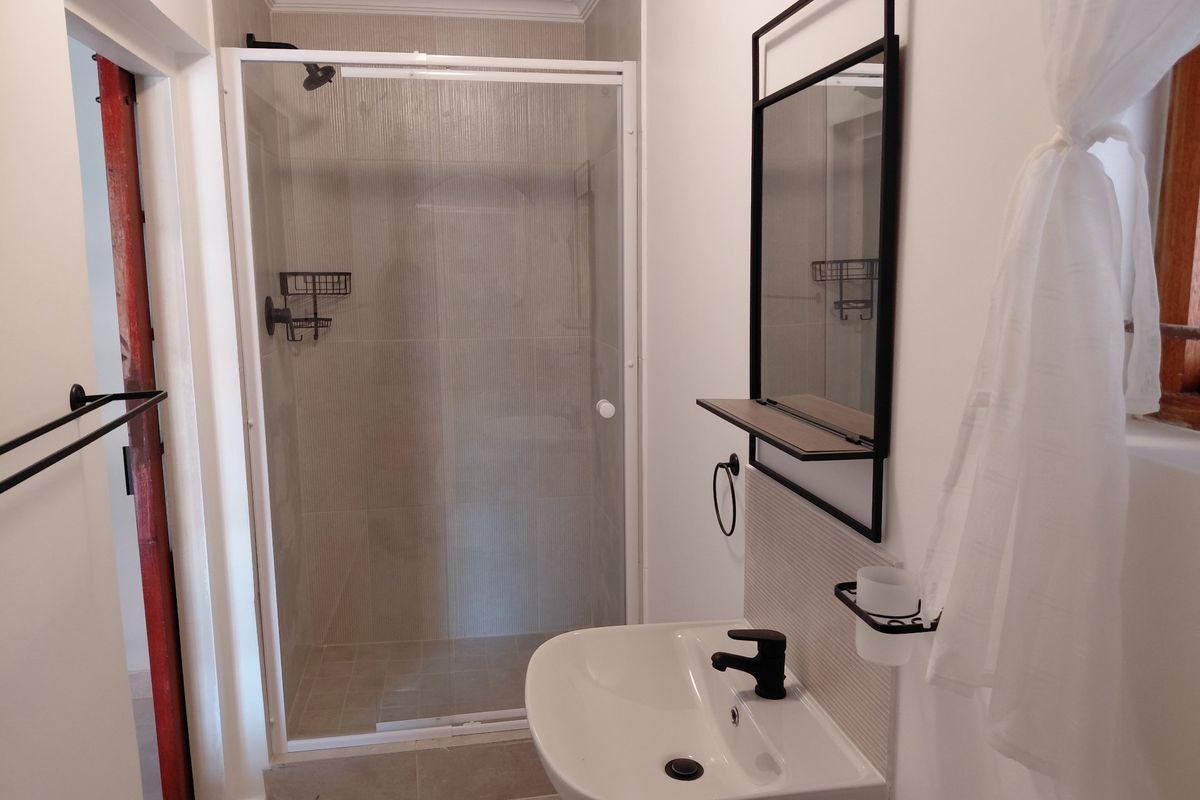 A clean, modern bathroom featuring a glass-enclosed shower, pedestal basin with a black mixer tap, and a matching wall-mounted mirror.