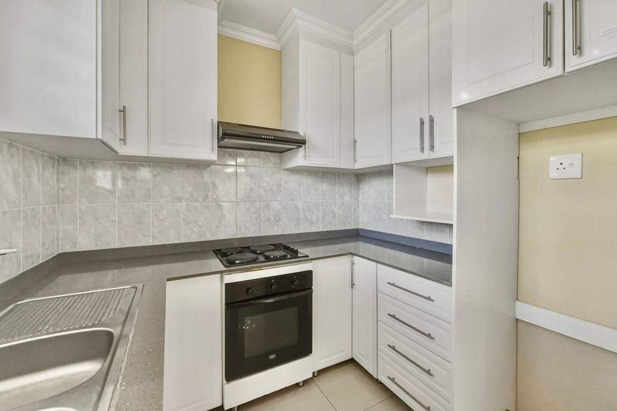 A clean, functional kitchen featuring white cabinetry, stone countertops, a built-in oven, electric hob, and a tiled backsplash.