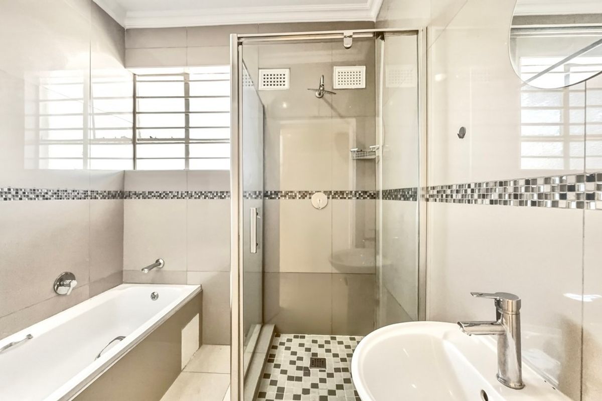 Modern bathroom featuring a built-in bathtub, separate glass shower enclosure, and a pedestal basin with neutral tiled finishes.