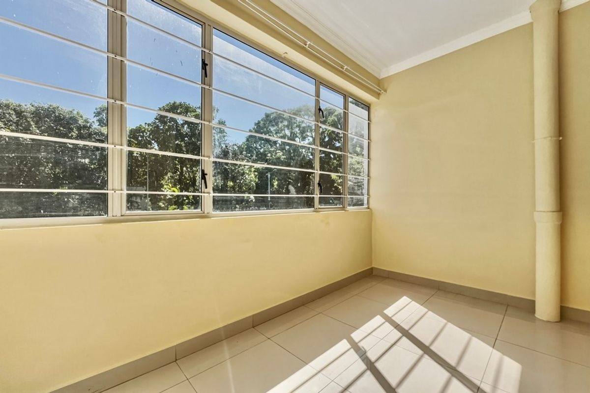 A bright, empty bedroom featuring large windows with security bars, tiled flooring, and neutral wall finishes, offering a clean canvas for personalization.