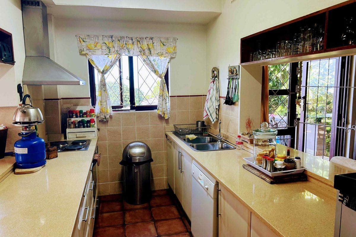 Functional kitchen featuring laminate countertops, tiled splashbacks, built-in cabinetry, and a stainless steel extractor fan, with direct access to the outdoor area.