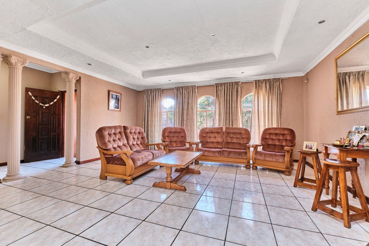 Spacious living room featuring tiled flooring, decorative columns, and a recessed ceiling with downlights, complemented by large arched windows.