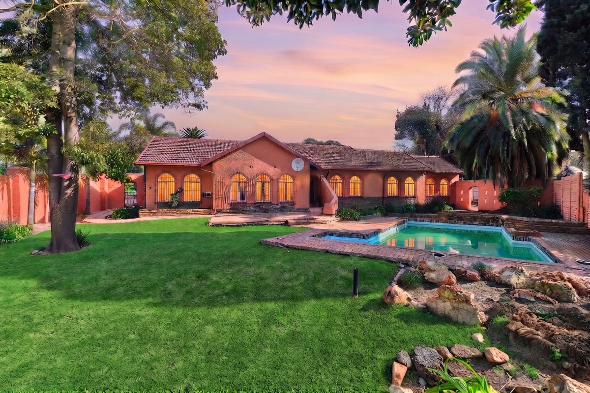 Rear view of a residential property featuring a swimming pool, landscaped garden, and distinctive arched windows set against a sunset sky.