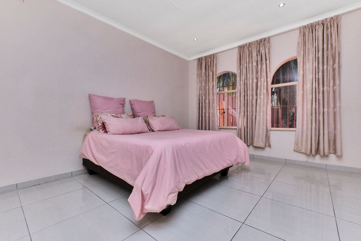 A bedroom featuring tiled flooring, arched windows with curtains, and recessed downlighting.