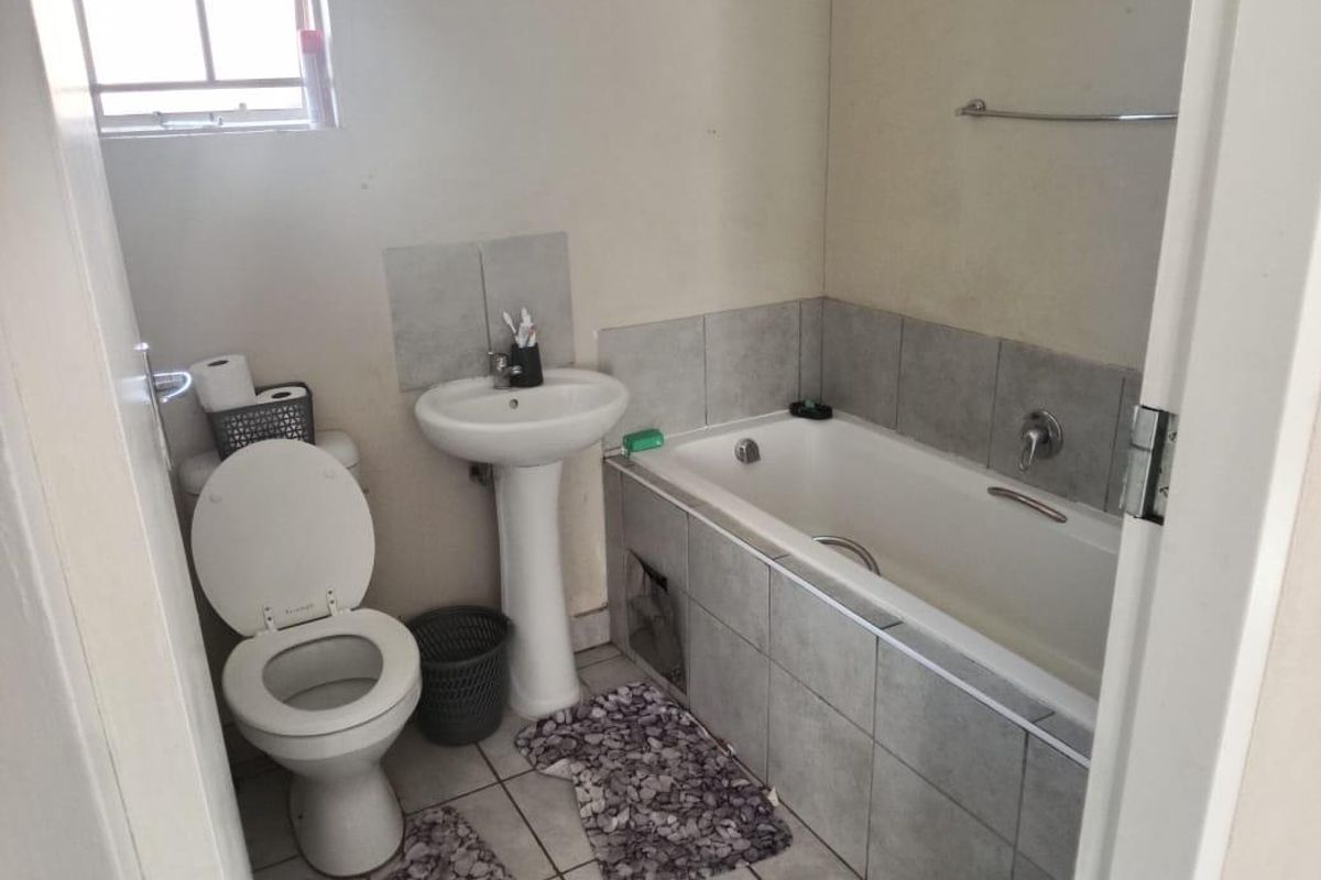 A functional bathroom featuring a pedestal basin, toilet, and bathtub with tiled splashbacks and flooring, requiring cosmetic updates to improve its overall condition.