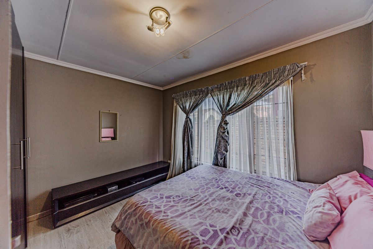 A bedroom featuring a built-in wardrobe, neutral wall tones, and a ceiling light fixture. Note the visible water stain on the ceiling.