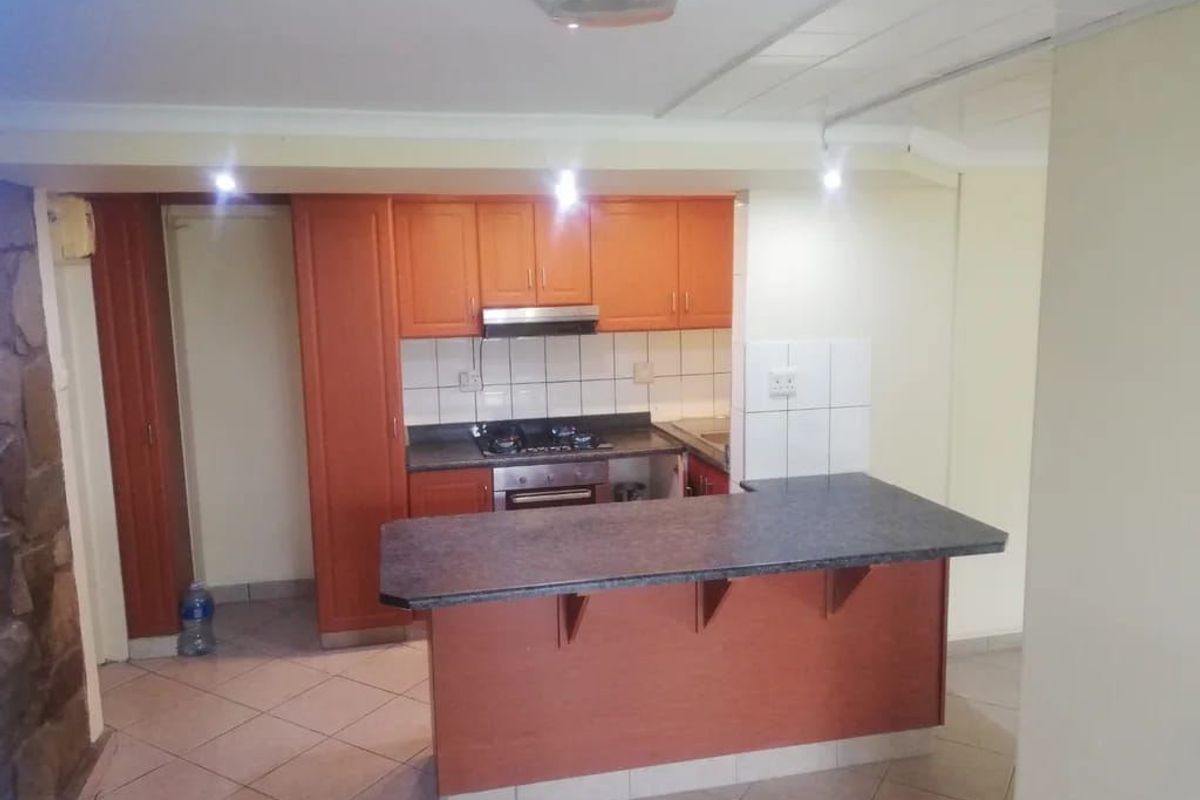 A functional kitchen featuring wooden cabinetry, a breakfast bar, built-in oven and hob, and tiled flooring, offering potential for modern updates.
