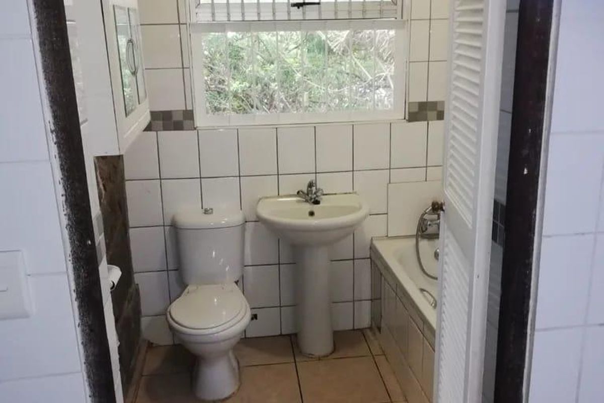 A compact bathroom featuring a pedestal basin, toilet, and bathtub with tiled finishes, requiring cosmetic updates to modernize the space.
