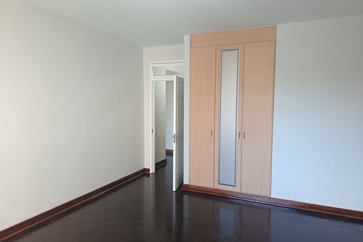 A bright, empty bedroom featuring polished parquet flooring and a built-in wardrobe with a central frosted glass panel.