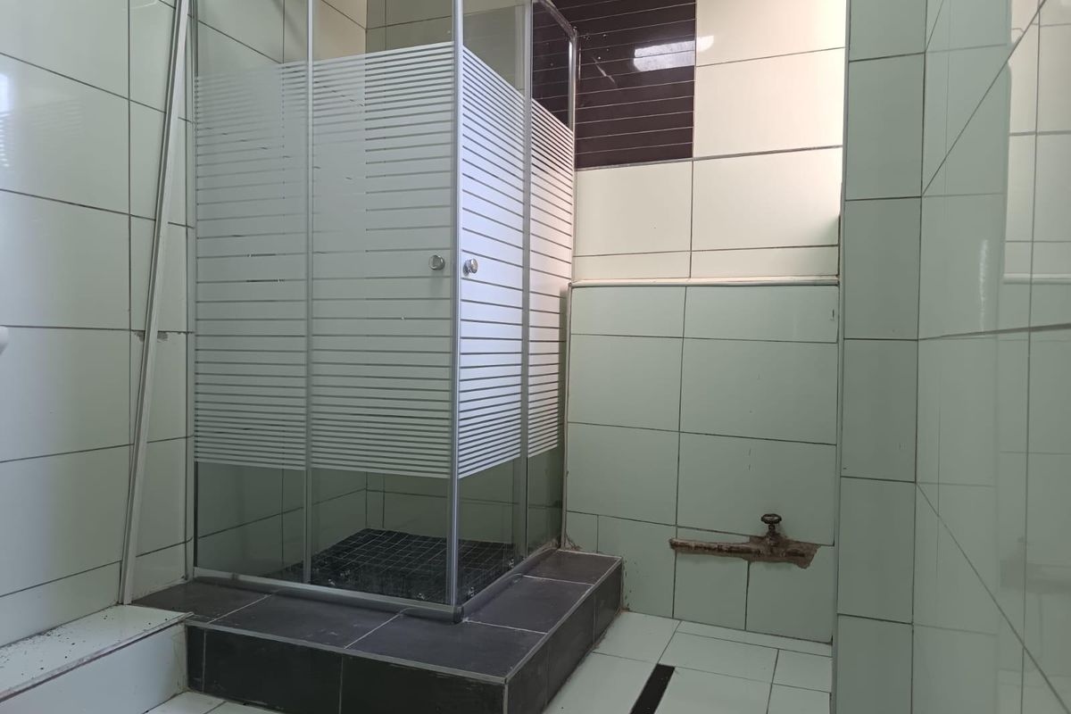 A bathroom featuring a glass shower enclosure with a rain shower head, tiled surfaces, and visible plumbing requiring maintenance or cosmetic repair.