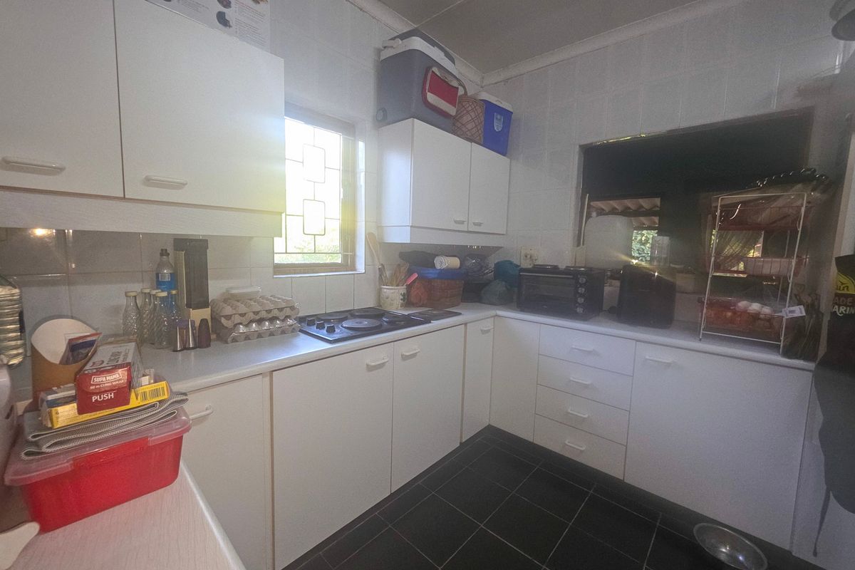 A functional kitchen featuring white built-in cabinetry, laminate countertops, an electric hob, and dark tiled flooring with a tiled splashback.