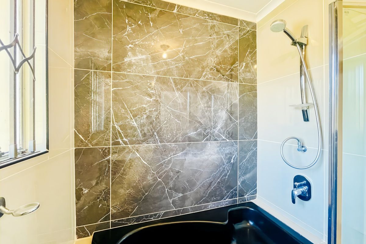 A bathroom featuring a built-in black bathtub with a marble-look tiled feature wall and a modern handheld shower fixture.