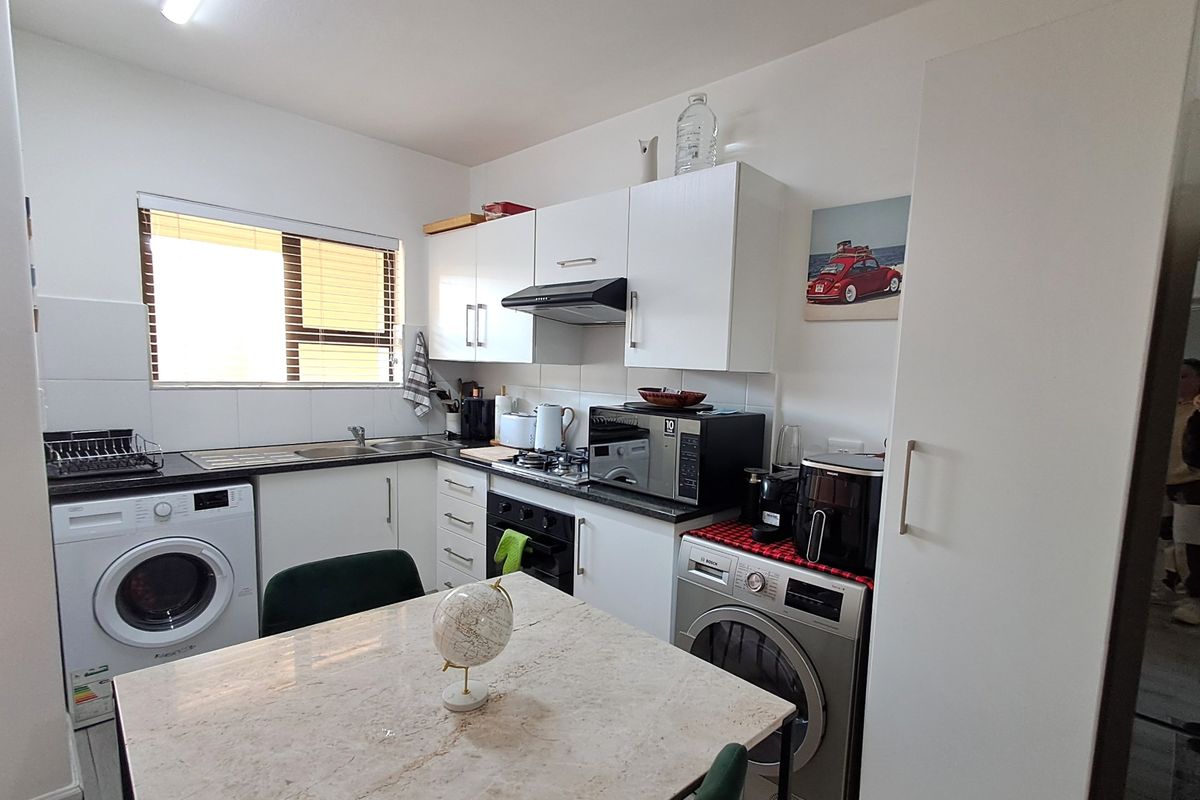 A functional kitchen featuring white cabinetry, built-in oven and hob, extractor fan, and integrated laundry appliances, providing a practical and efficient workspace.