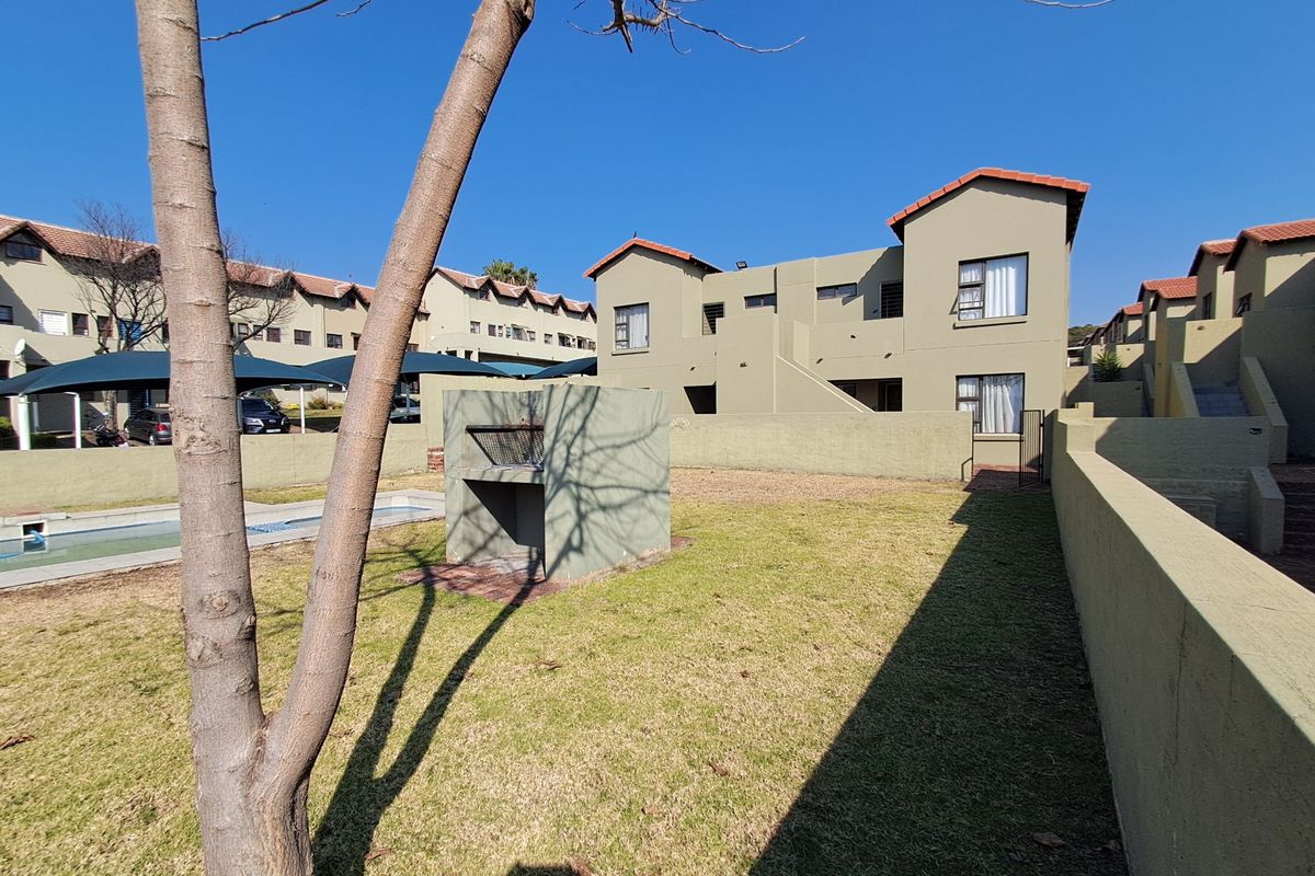 Rear exterior view of the apartment complex featuring a communal garden, built-in braai area, and swimming pool with surrounding boundary walls.