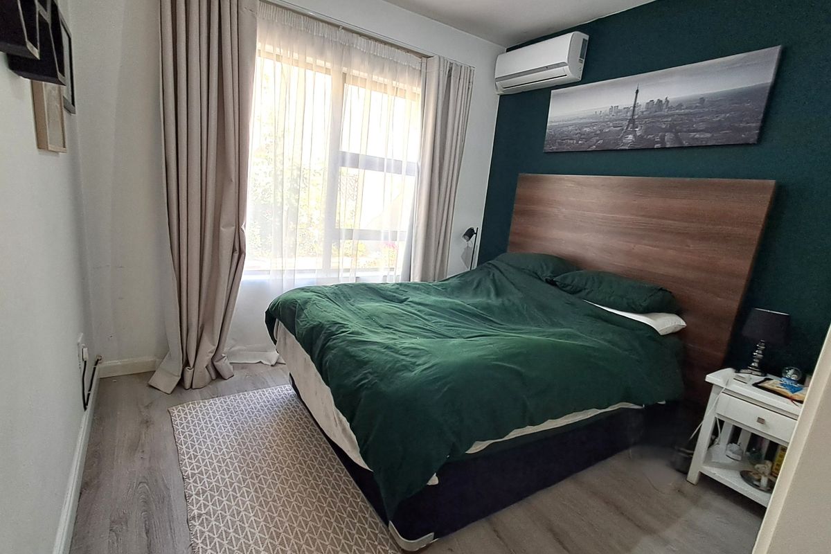 A well-maintained bedroom featuring laminate flooring, a wall-mounted split-system air conditioner, and large windows with curtain tracks.