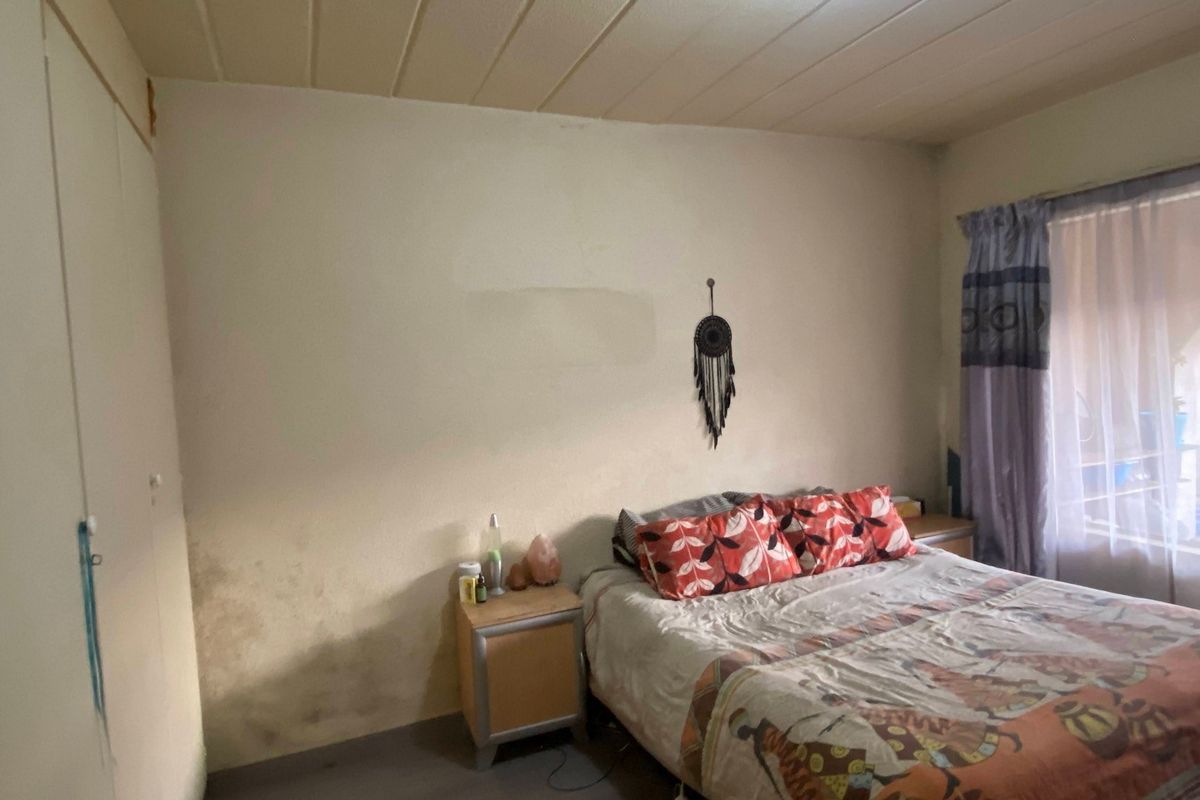 A bedroom featuring a built-in wardrobe and panel ceiling, currently showing signs of wall staining and wear requiring cosmetic attention.