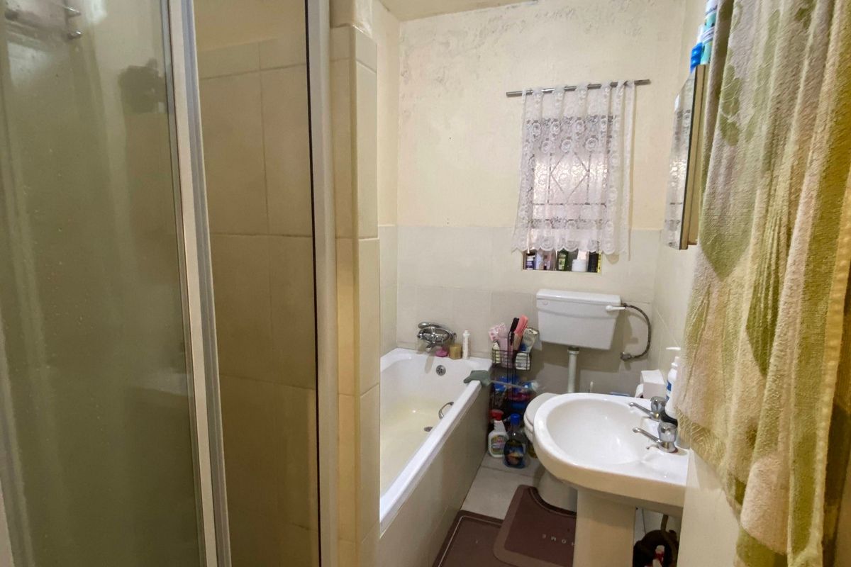 A compact bathroom featuring a shower enclosure, bathtub, pedestal basin, and toilet, requiring cosmetic updates to the wall and ceiling finishes.
