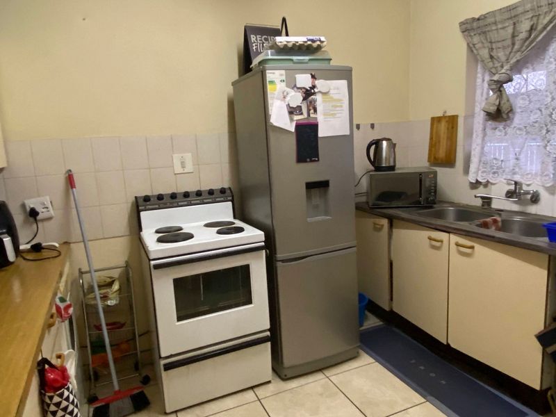 A compact kitchen featuring dated cabinetry, tiled splashbacks, a double bowl sink, and a freestanding electric stove with tiled flooring.