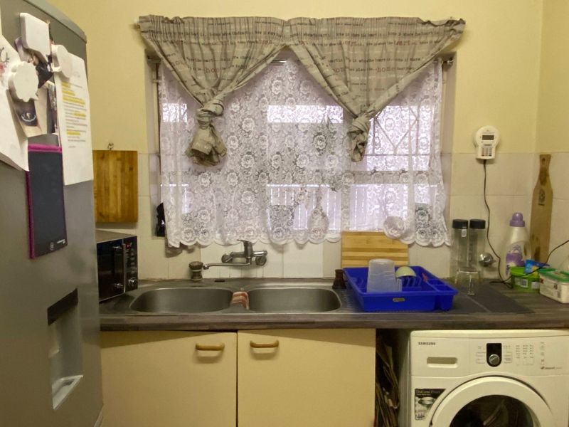 A functional kitchen area featuring a double bowl stainless steel sink, laminate countertops, tiled splashback, and built-in base cabinetry.