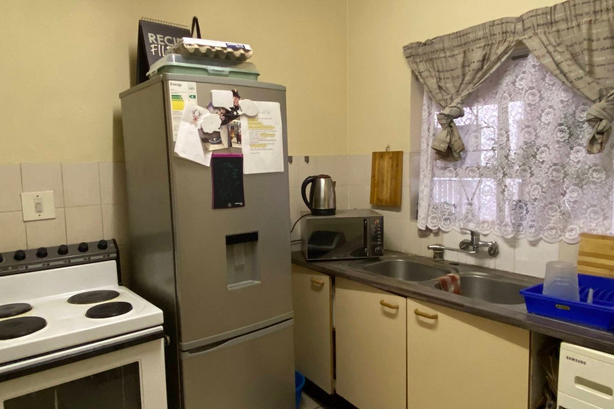 A compact kitchen featuring a freestanding electric stove, double bowl sink, laminate countertops, and built-in cabinetry with a tiled splashback.