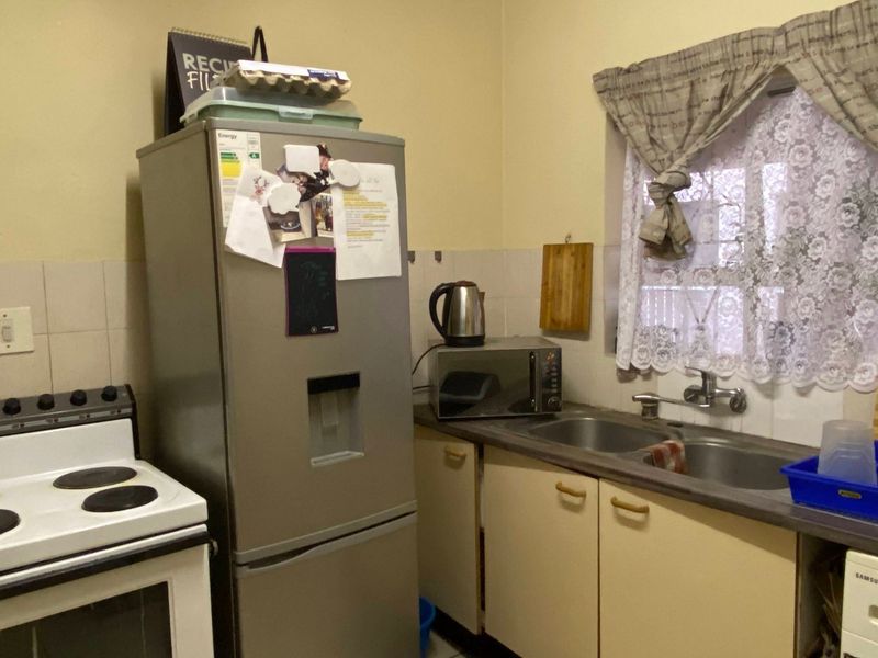 A compact kitchen featuring a freestanding electric stove, double bowl sink, laminate countertops, and built-in cabinetry with a tiled splashback.