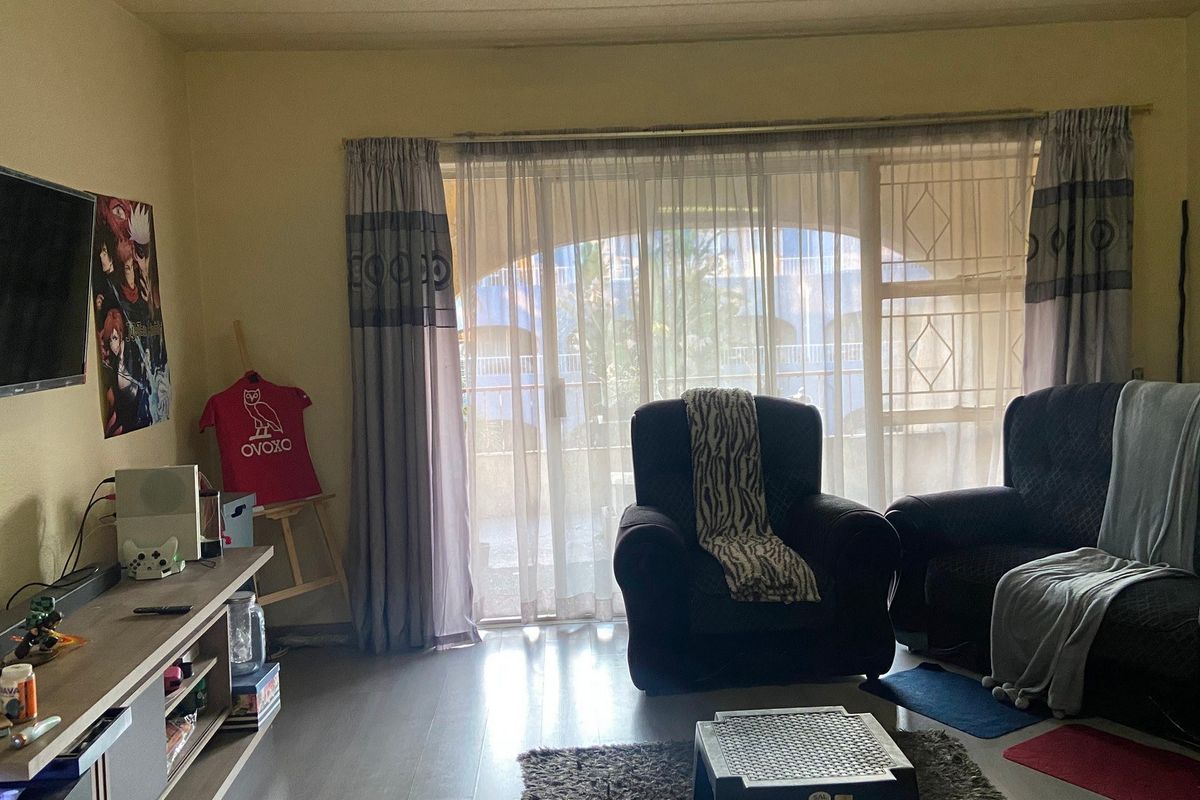 A living room featuring laminate flooring and a large sliding glass door with an integrated security gate, providing access to the exterior.