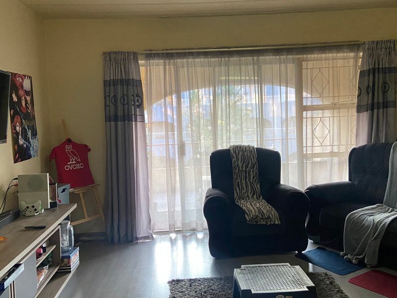 A living room featuring laminate flooring and a large sliding glass door with an integrated security gate, providing access to the exterior.