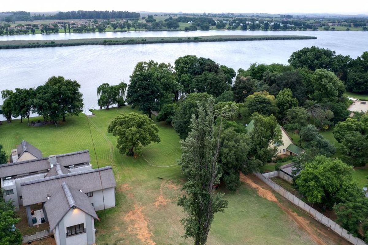 Aerial view of a spacious property featuring a thatched-roof residence, expansive landscaped grounds, and direct river frontage.