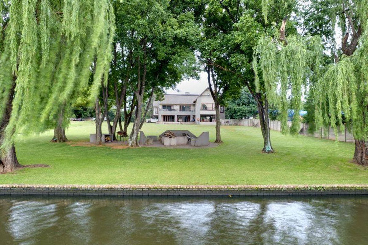 A spacious rear garden featuring a built-in fire pit area, mature trees, and direct waterfront access, providing a serene outdoor setting.