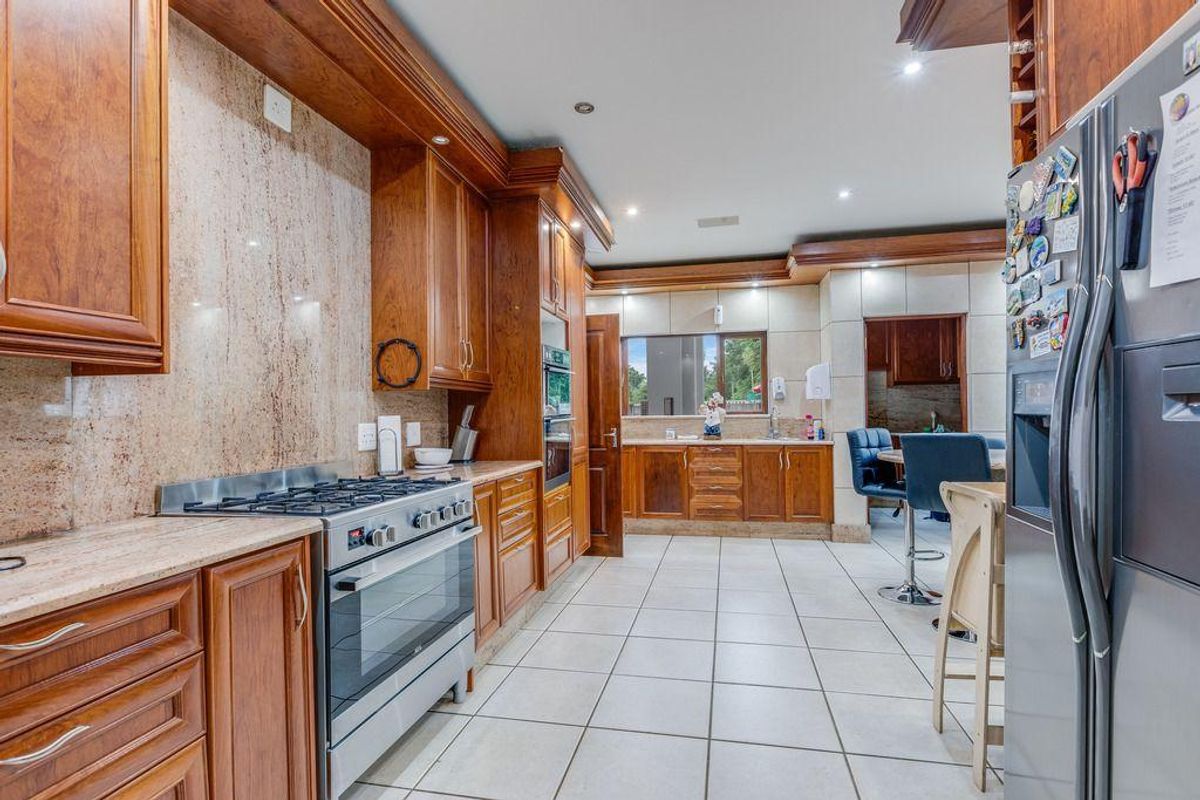Spacious kitchen featuring warm-toned wooden cabinetry, stone countertops, a gas stove, and tiled flooring, with an open layout connecting to an adjacent dining area.