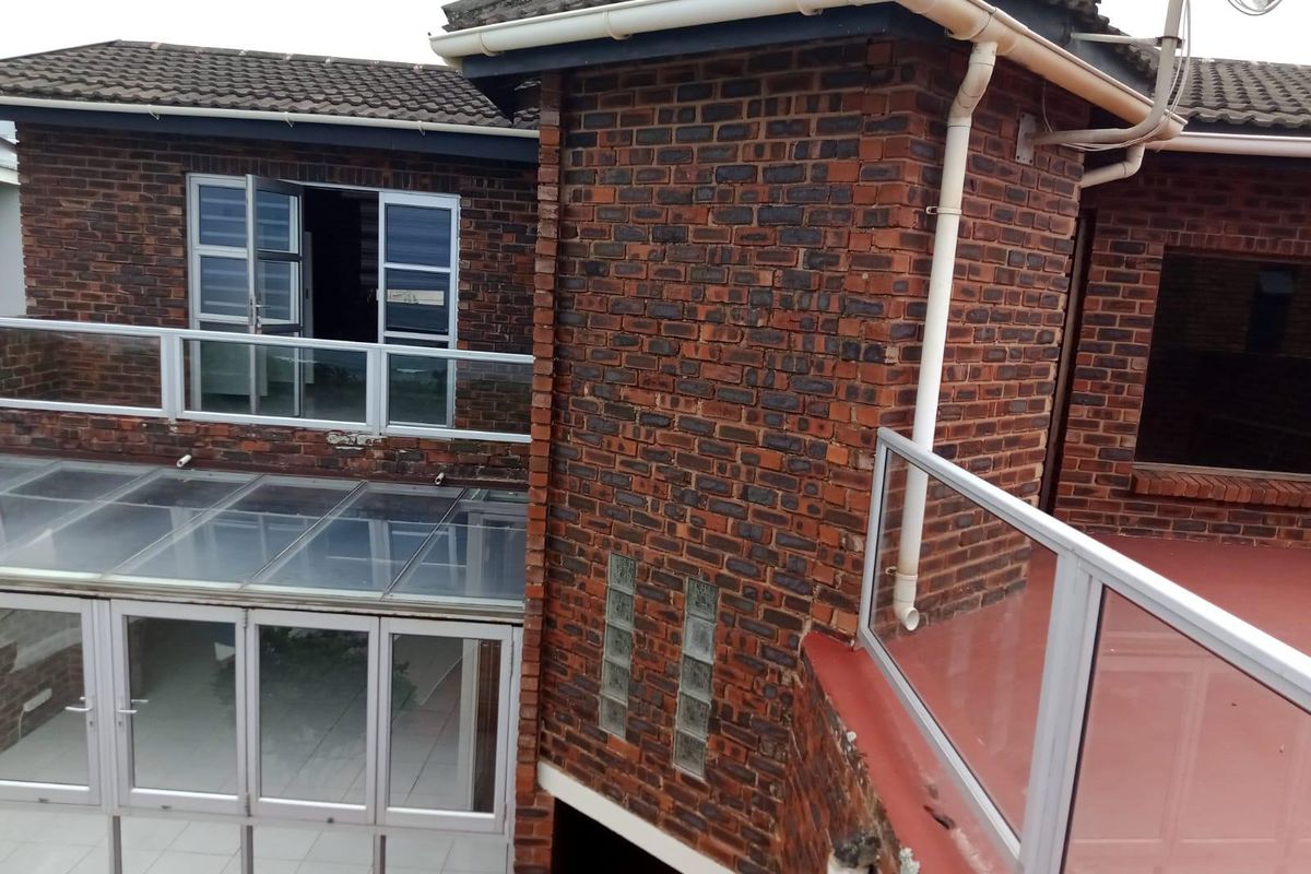 Rear exterior view of a multi-level face brick house featuring glass balustrades, a glass-roofed patio area, and tiled roofing.