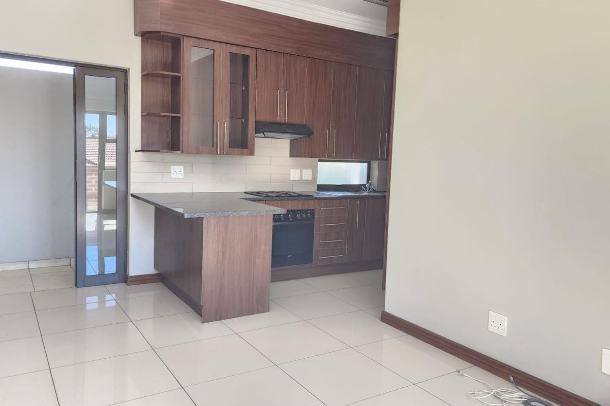 Modern kitchen featuring dark wood cabinetry, granite countertops, built-in oven, gas hob, and tiled flooring, leading to an adjacent utility area.