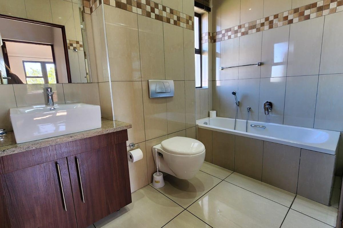 A well-maintained bathroom featuring a wall-mounted toilet, built-in bathtub, vanity cabinet with a vessel sink, and neutral tiled finishes.