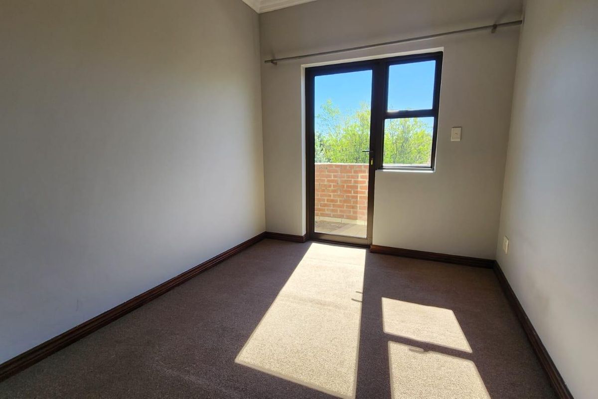 A bright, empty bedroom featuring neutral walls, carpeted flooring, and a glass door providing direct access to an outdoor balcony area.