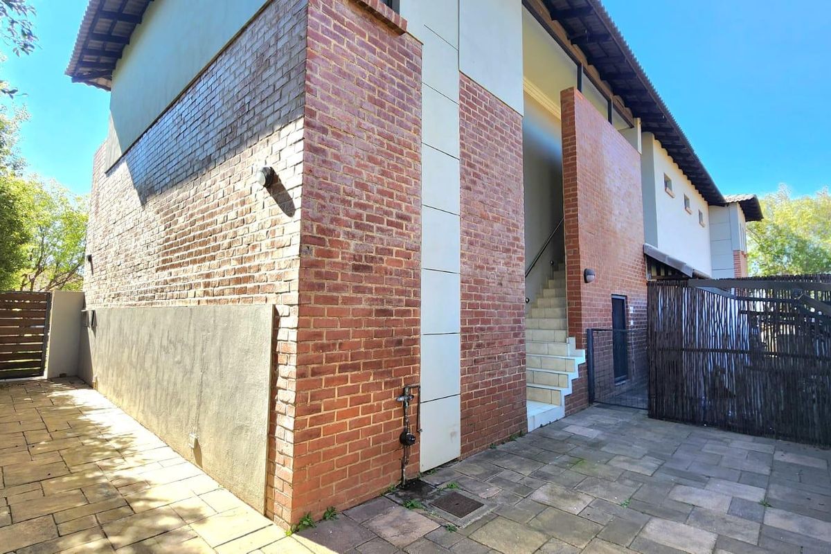 Rear exterior view of the apartment building featuring a brick facade, paved courtyard area, and an external staircase leading to the upper level.
