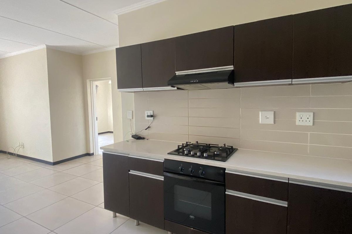 A clean, modern kitchen featuring dark cabinetry, a gas hob, built-in oven, extractor fan, and neutral tiled flooring.